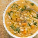 A top view of a white bowl full of white bean soup over a wooden background.