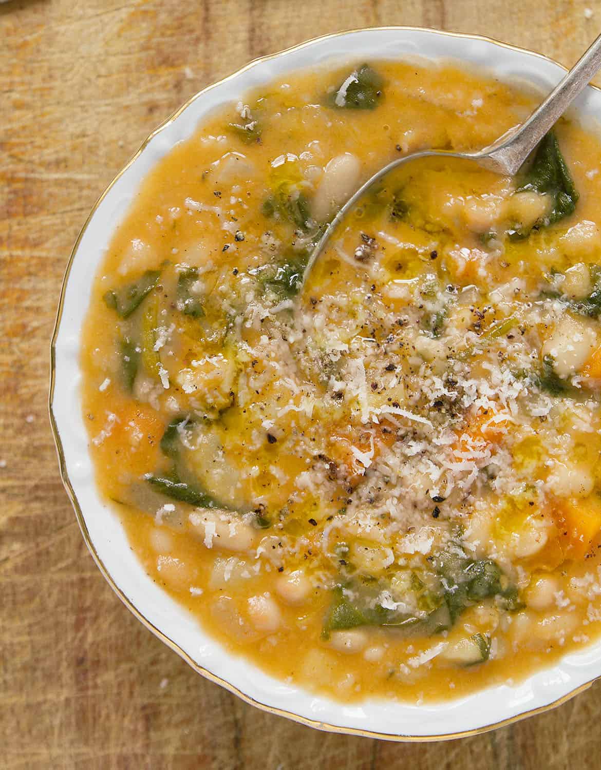 A white bowl full of white bean soup with grated parmesan cheese over a wooden table.