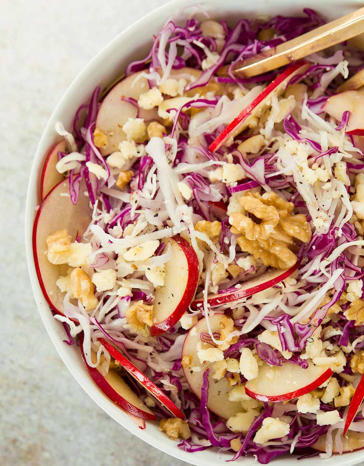 Cabbage salad with apples and walnuts in a white bowl with a golden spoon - The Clever Meal