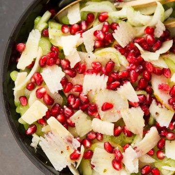 A black bowl of celery salad with parmesan and pomegranate.