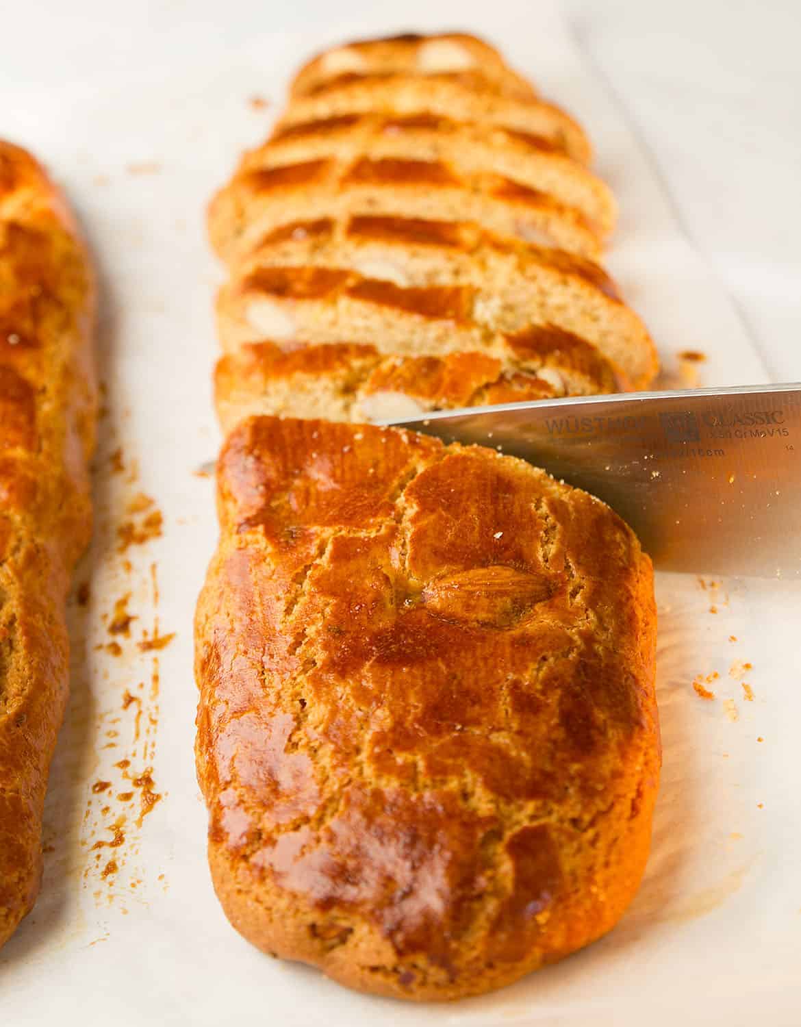 A knife cutting one of the almond biscotti logs into slices.