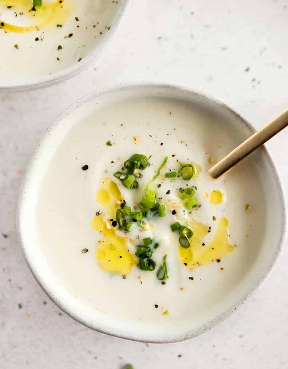 A white bowl of creamy cauliflower decorated with olive oil and chopped spring onions - Real + Vibrant
