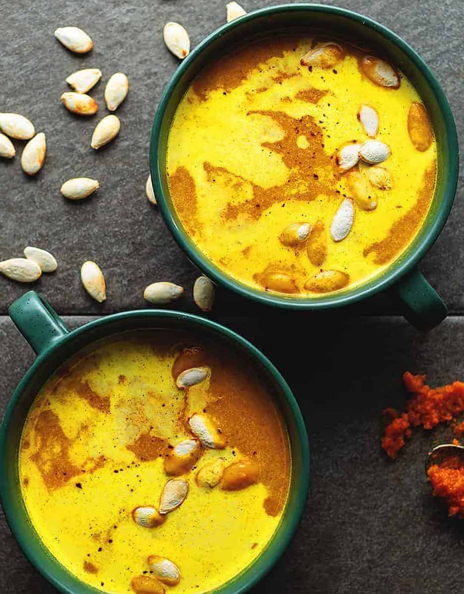 Two bowls with curried pumpkin soup and pumpkin seeds on a black background - Jennifer Banz