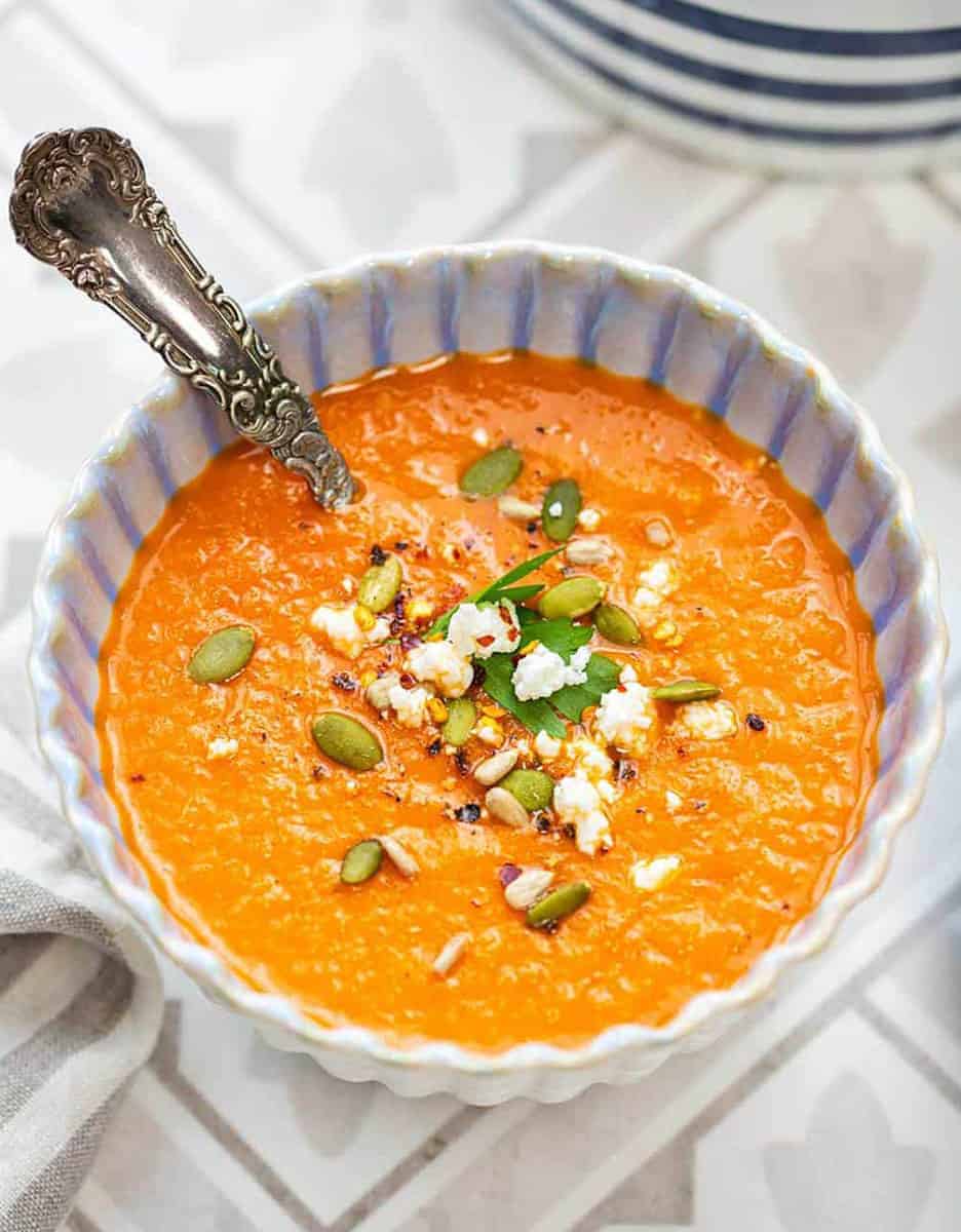 Tomato soup with pumpkin seeds in a white bowl with a spoon - Supergolden Bakes