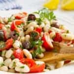Cannellini bean salad on a white plate with a wooden spoon.