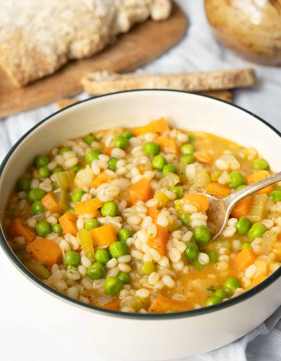 Vegetable barley in a white bowl with a spoon. Bread on the background.