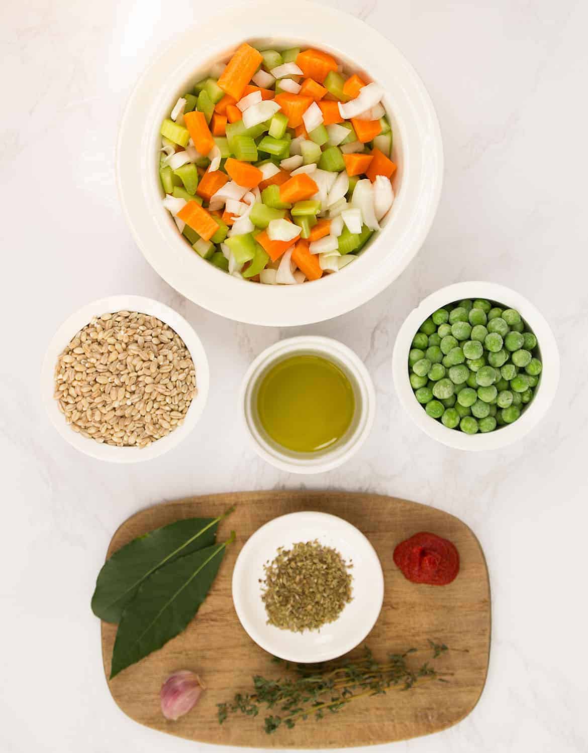 The ingredients to make this barley soup are arranged on a white marble table.