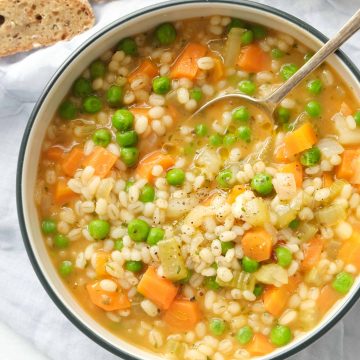 Vegetable barley soup in a white bowl with a metal spoon.