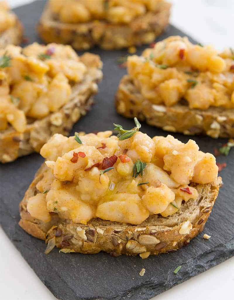 Little toasts topped with smocked beans on a black slate tray - The Clever Meal