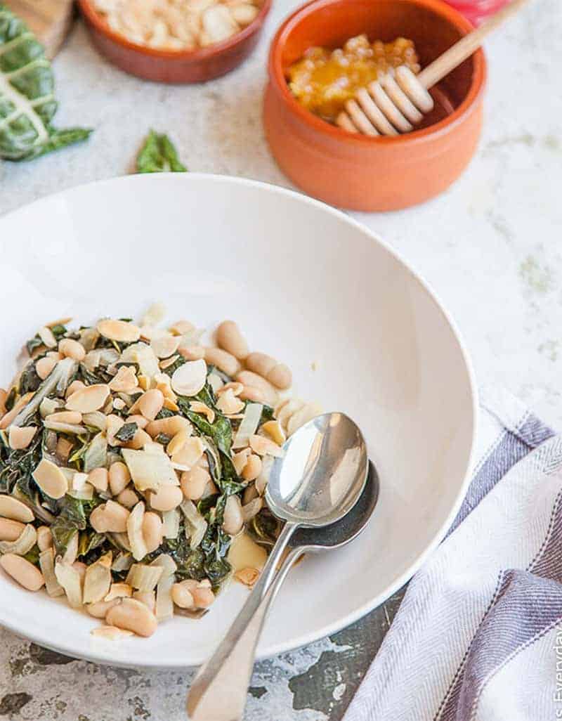 Silverbeet with cannellini beans, honey, and almonds  on a white plate - Delicious Everyday
