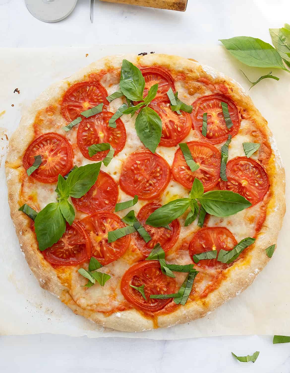 A caprese pizza on a white background with fresh basil leaves.