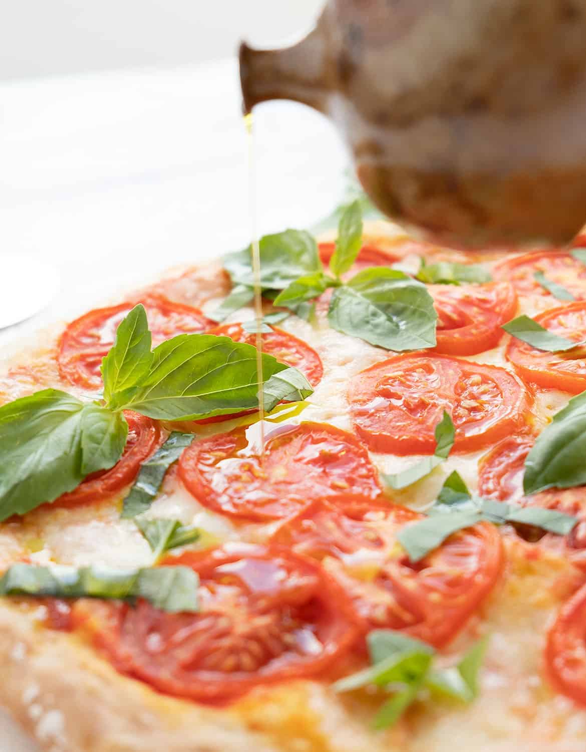 A drizzle of extra virgin olive oil over a freshly baked caprese pizza.