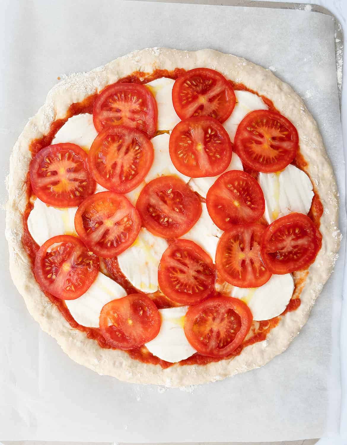 A pizza caprese with slices of tomato and mozzarella before baking.