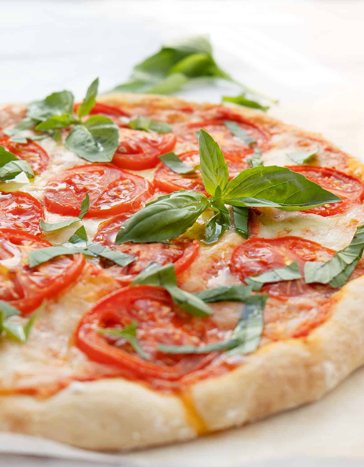 A delicious Caprese pizza on a white plate with green basil leaves.