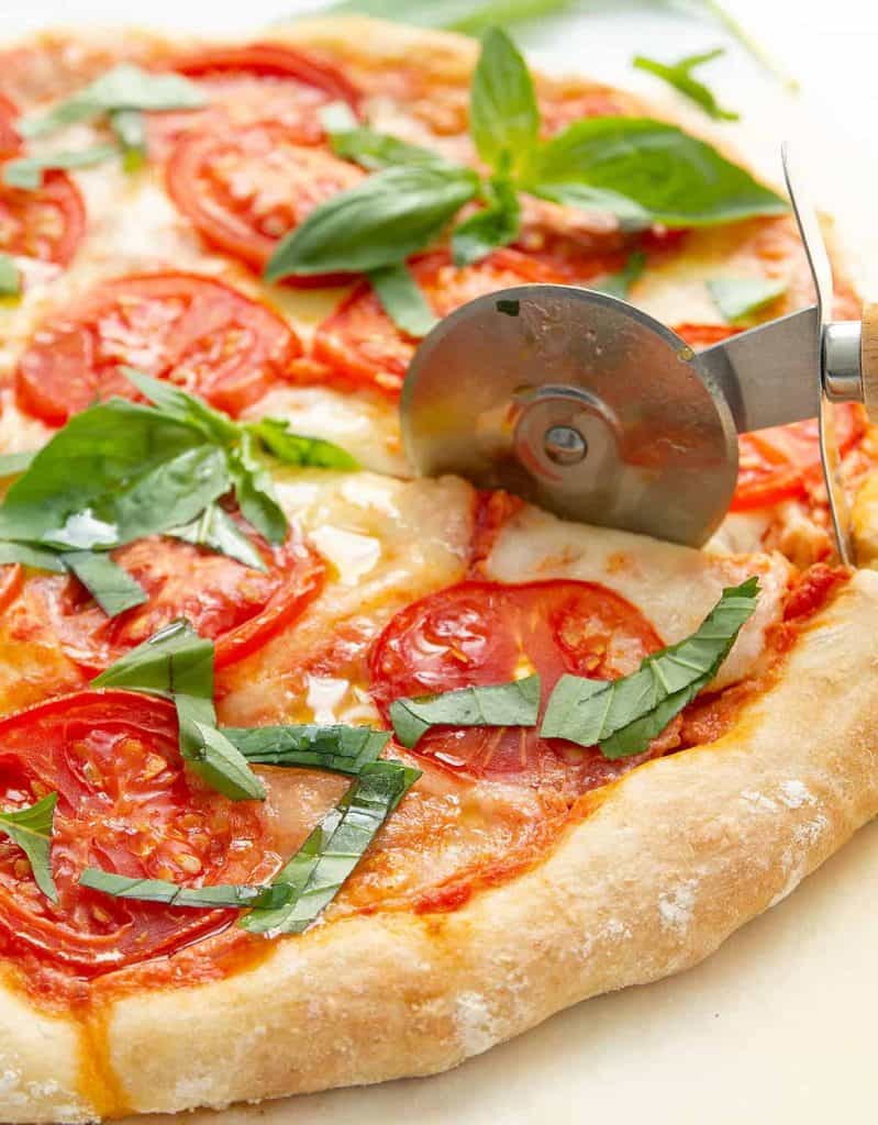 A pizza cutter is cutting a slice of caprese pizza.