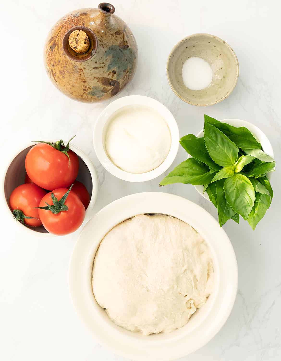 The ingredients to make this caprese pizza are arranged on a white marble table.