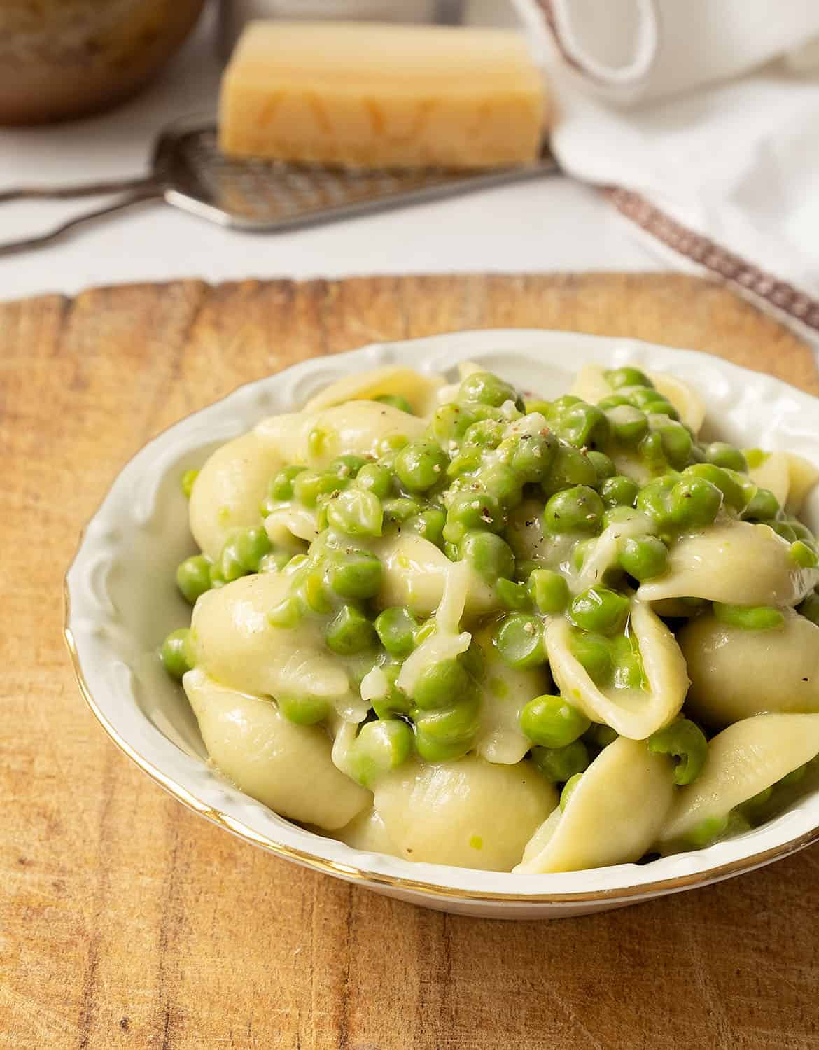 A white bowl with pasta with peas on a wooden table.