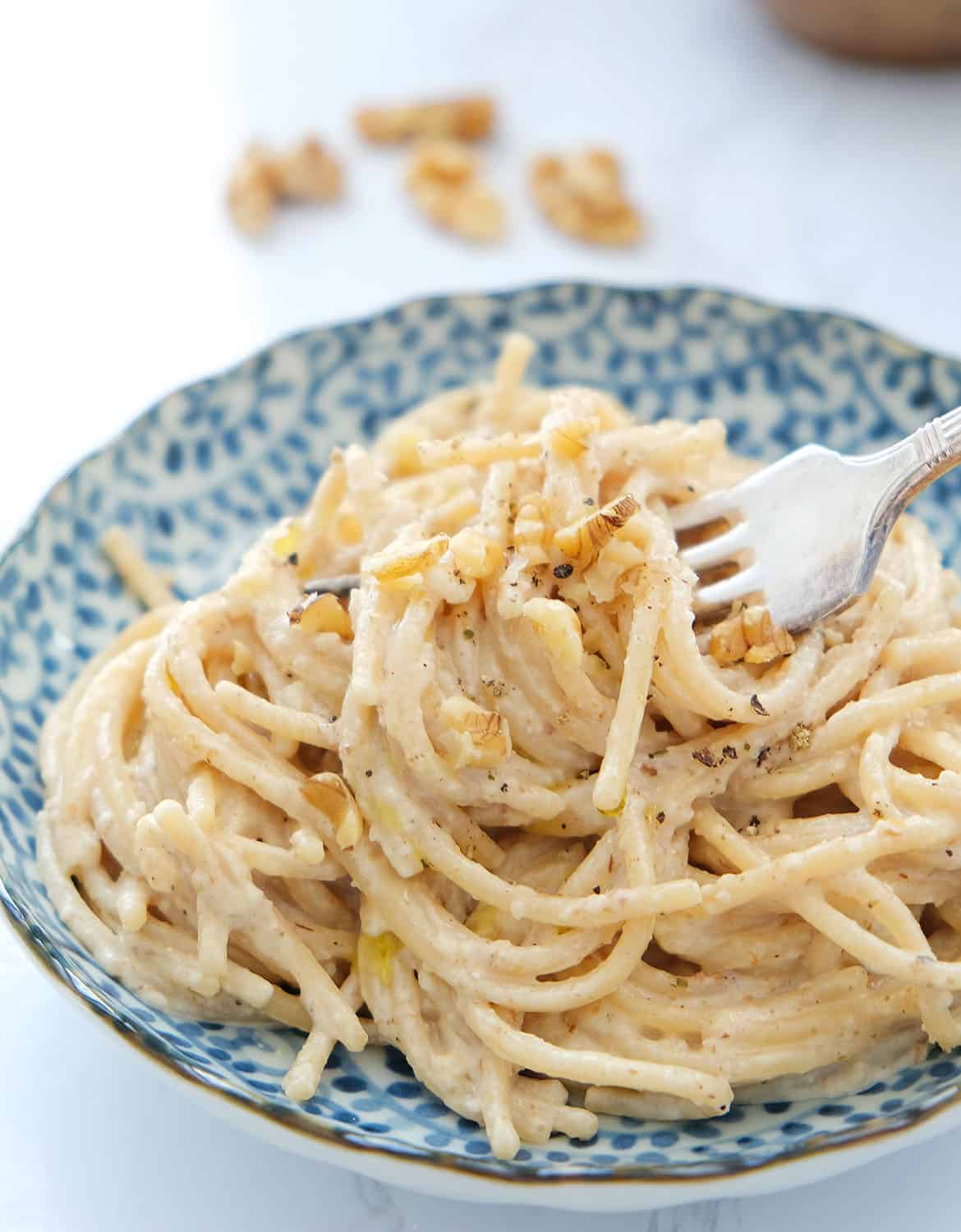 A fork is lifting some spaghetti with walnut sauce served in a blue bowl.