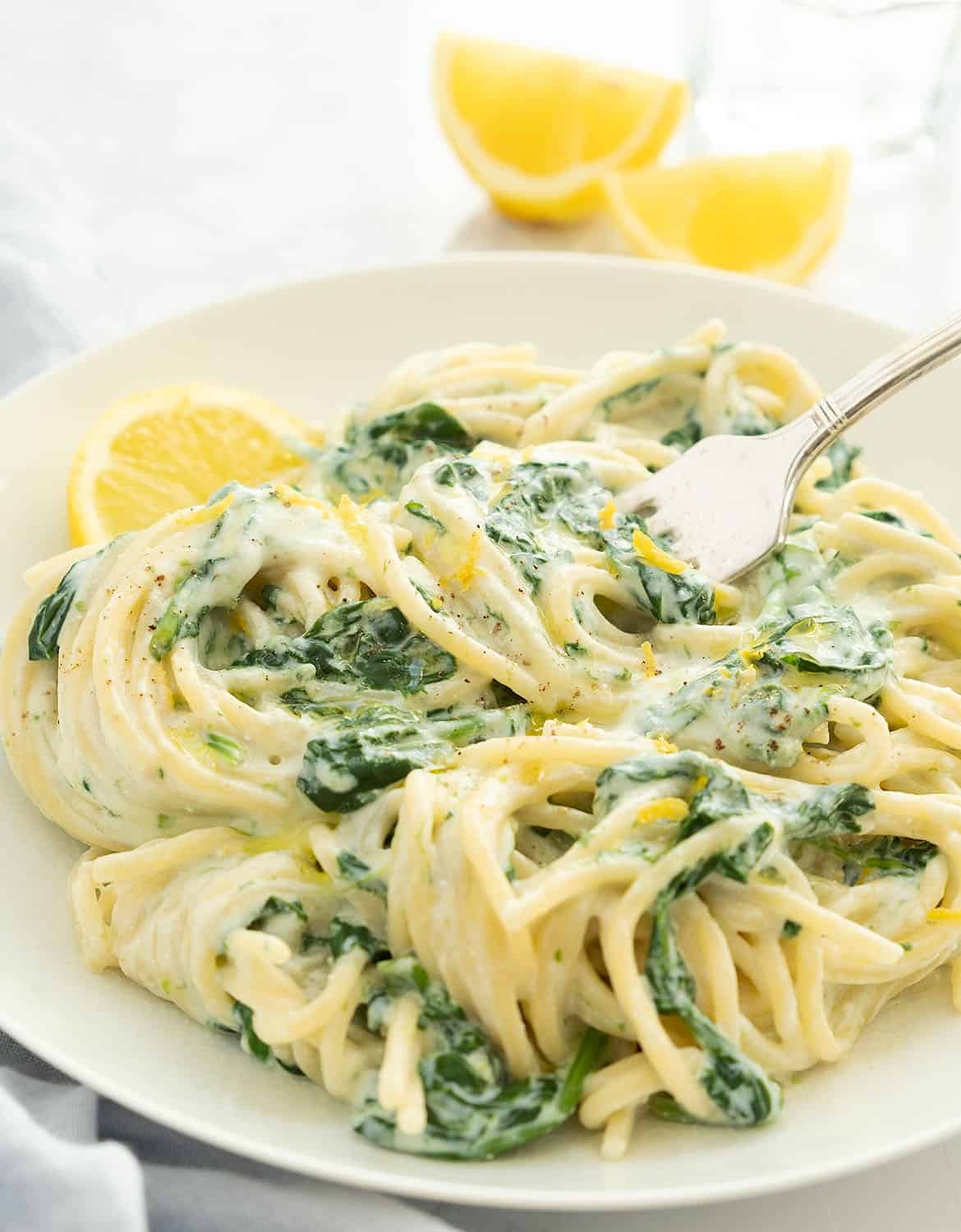 Lemon ricotta pasta with spinach and lemon wedges on a white background.