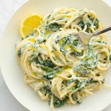 Creamy lemon ricotta pasta with spinach on a white plate.