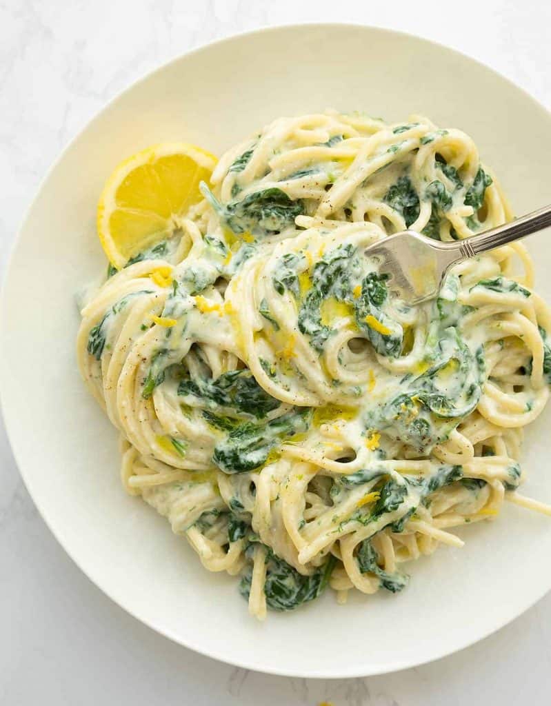 Creamy lemon ricotta pasta with spinach on a white plate.
