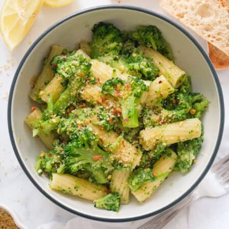 Top view of a bowl full of pasta with broccoli topped with breadcrumbs and chili flakes.