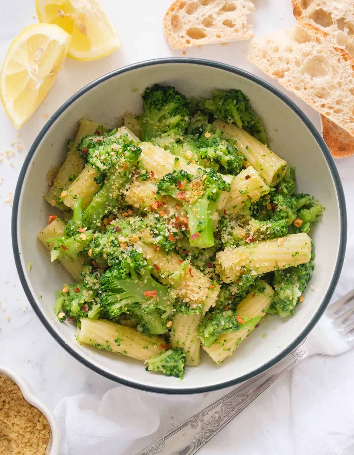 Top view of a bowl full of pasta with broccoli topped with breadcrumbs and chili flakes.