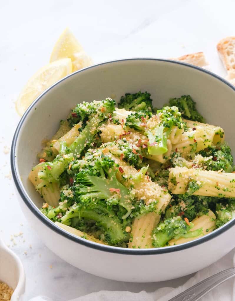 Close-up of a bowl full of pasta with broccoli over a white background.