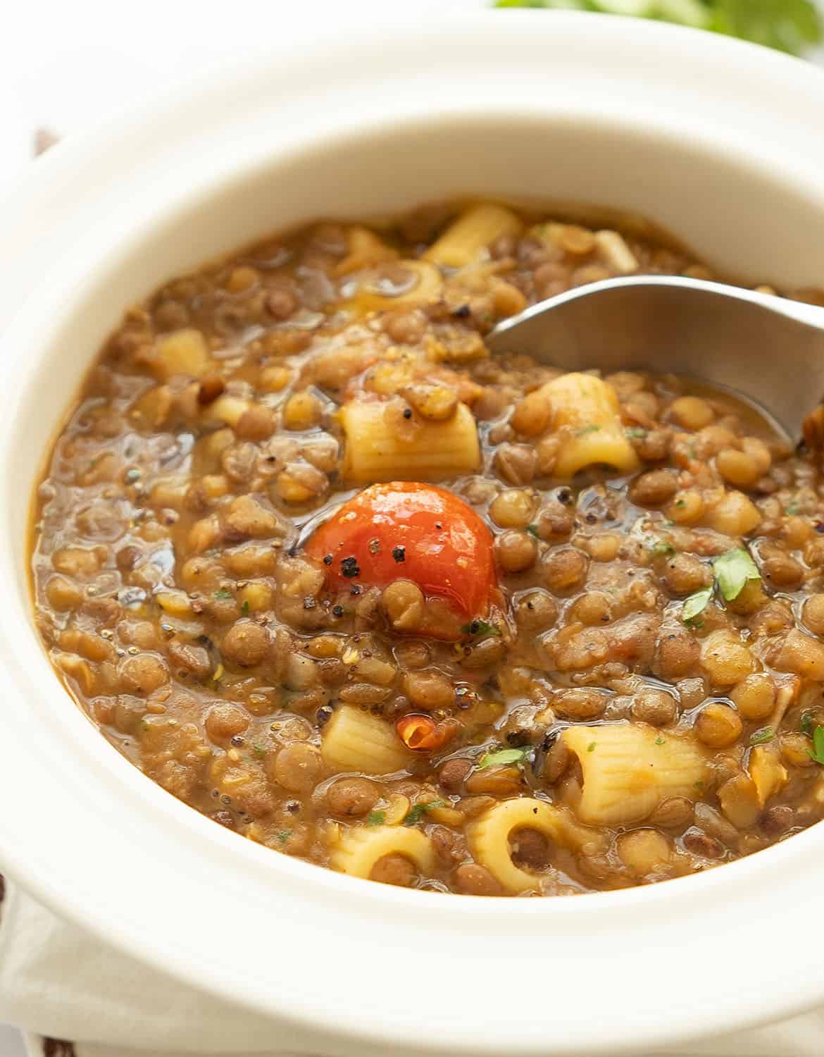 Pasta with lentils served in a white bowl with a spoon.