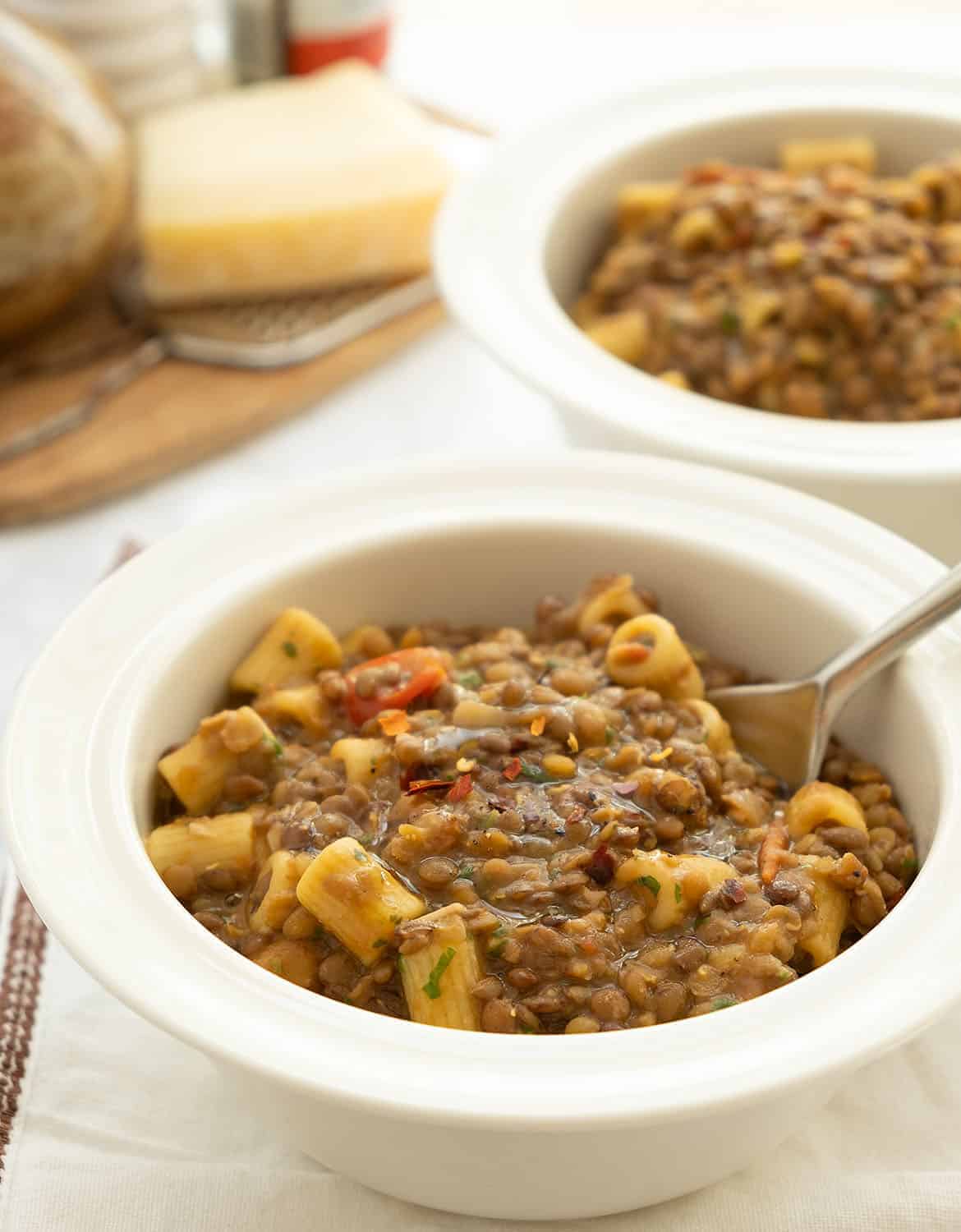 A white table and two white bowls full of pasta with lentils.