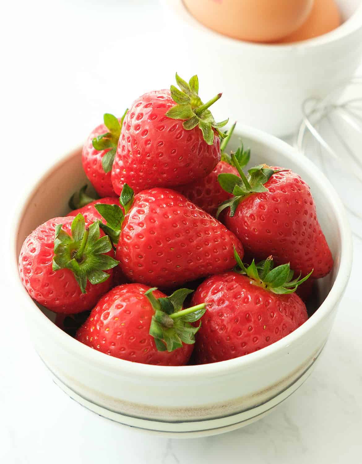 Strawberries in a bowl, in the background a small white bowl containing eggs.