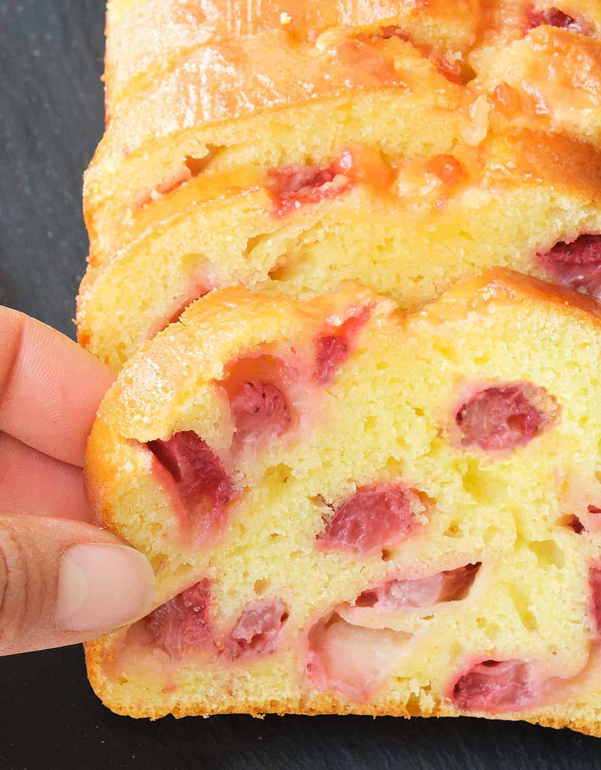 A hand is grabbing the first slice of a moist strawberry bread.