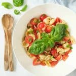 Tomato pasta salad with large basil leaves in a white salad bowl.