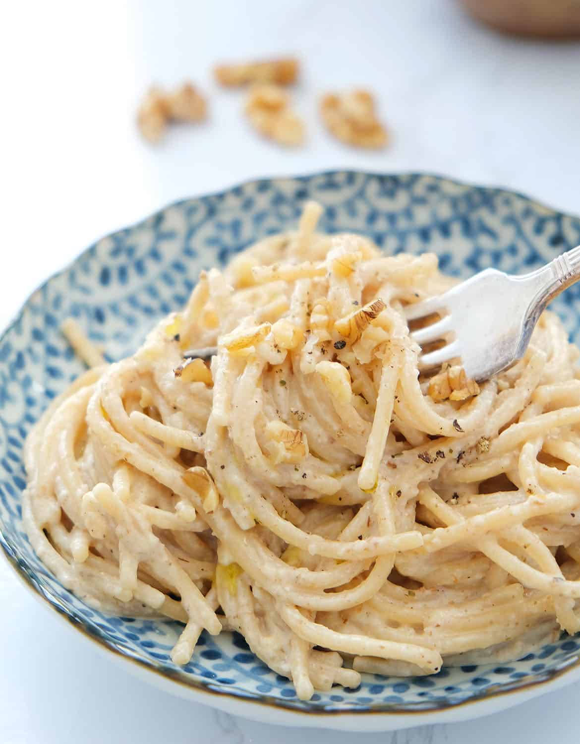 Easy spaghetti with walnut sauce and chopped walnuts in a blue bowl with a fork.