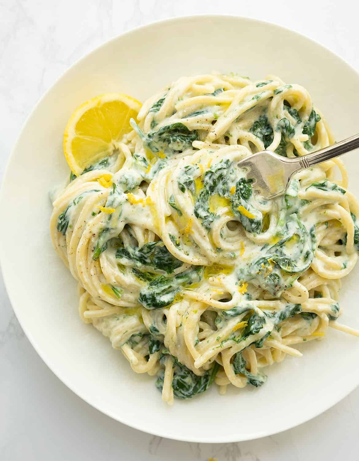 Quick spaghetti with ricotta, spinach and a slice of lemon on a white plate.