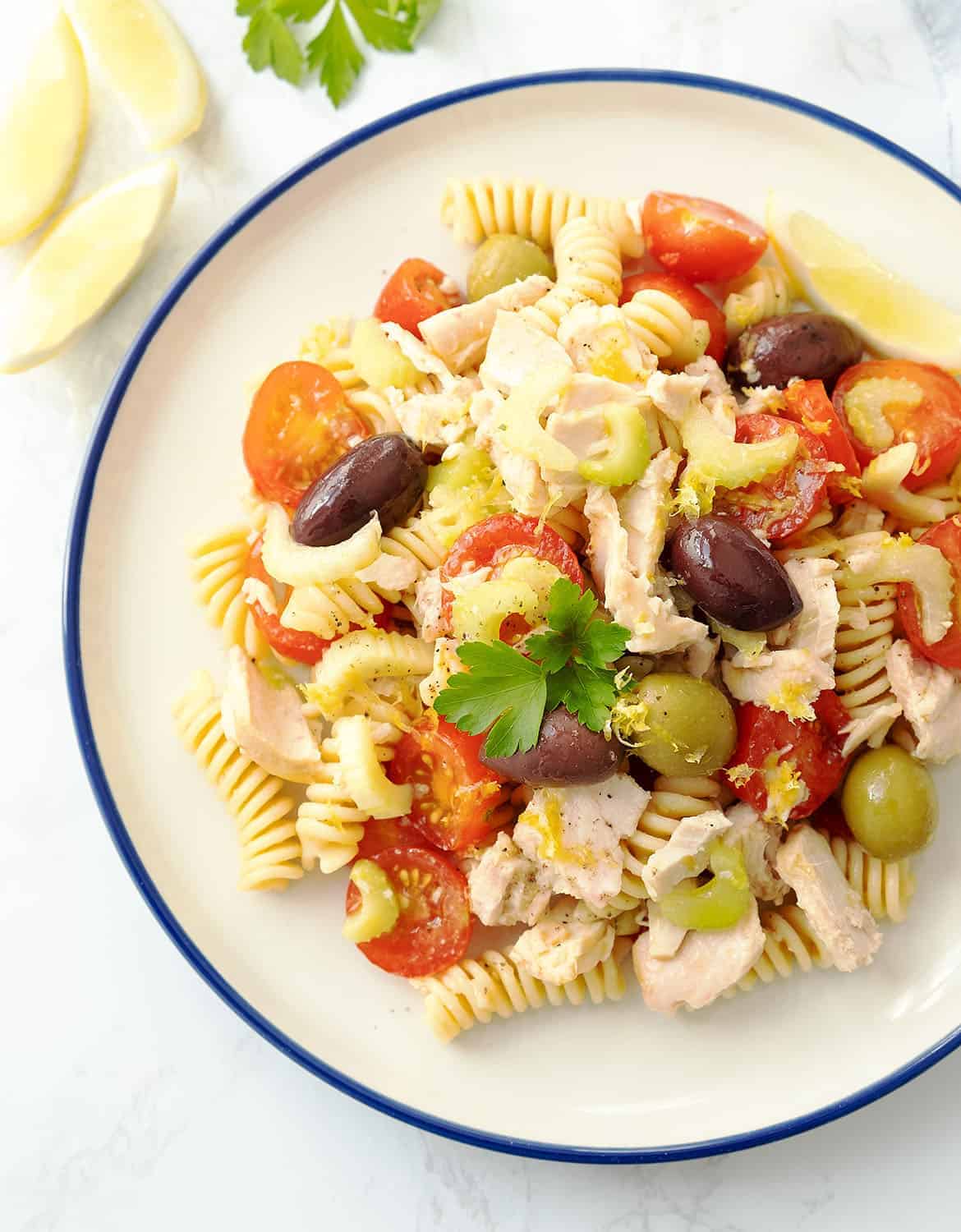 Tuna pasta salad with cherry tomatoes and olives on a white plate with a blue rim.