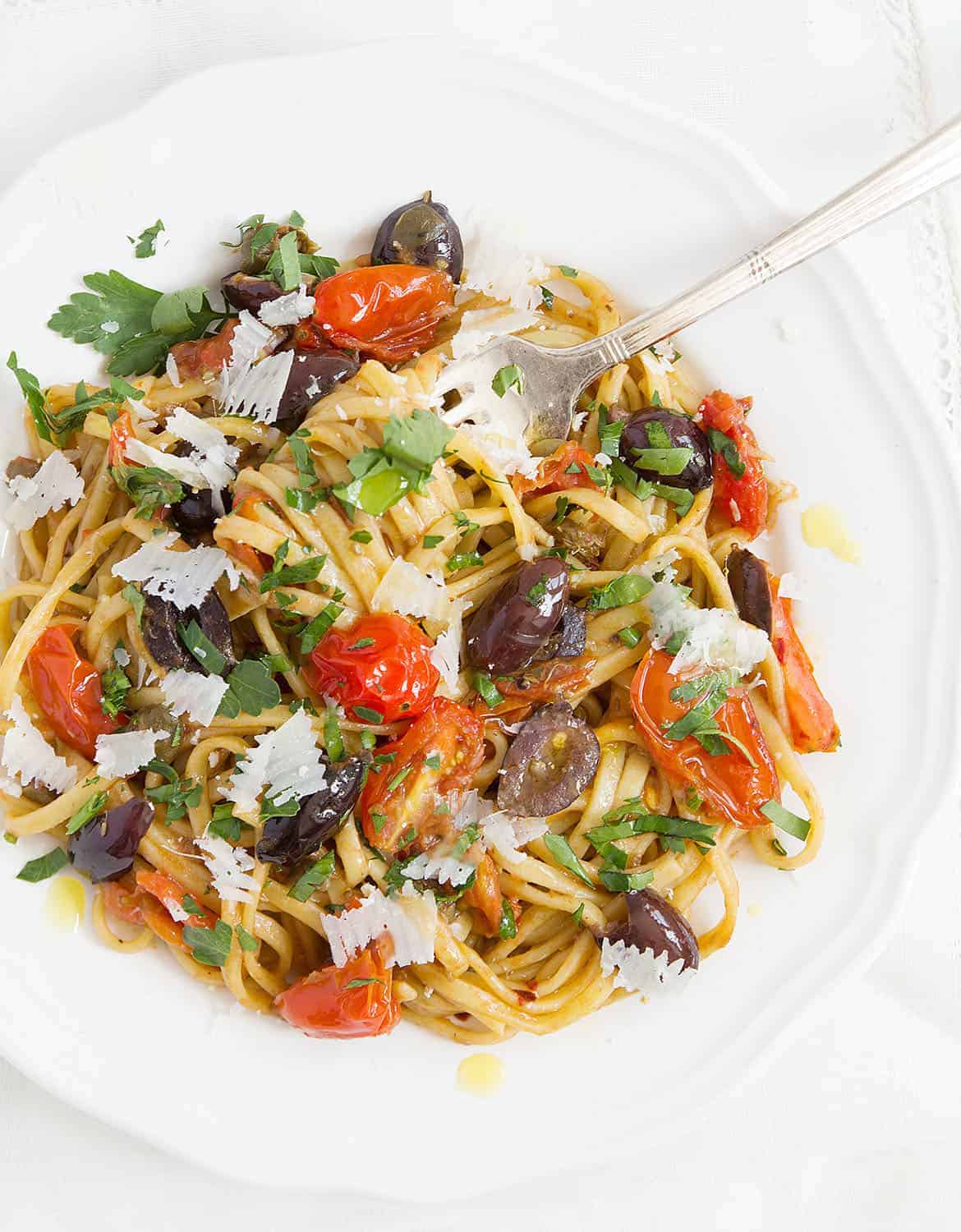 Quick pasta recipe with olives, tomatoes, parsley leaves on a white plate.