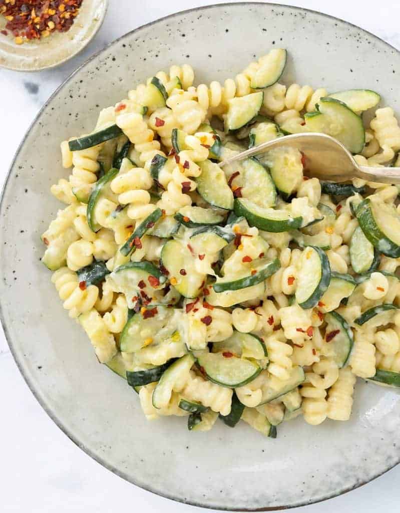 Creamy pasta with zucchini with a pinch of chili flakes on a grey plate.
