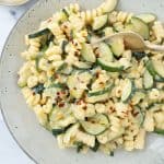 Creamy pasta with zucchini with red chili flakes on a grey plate.