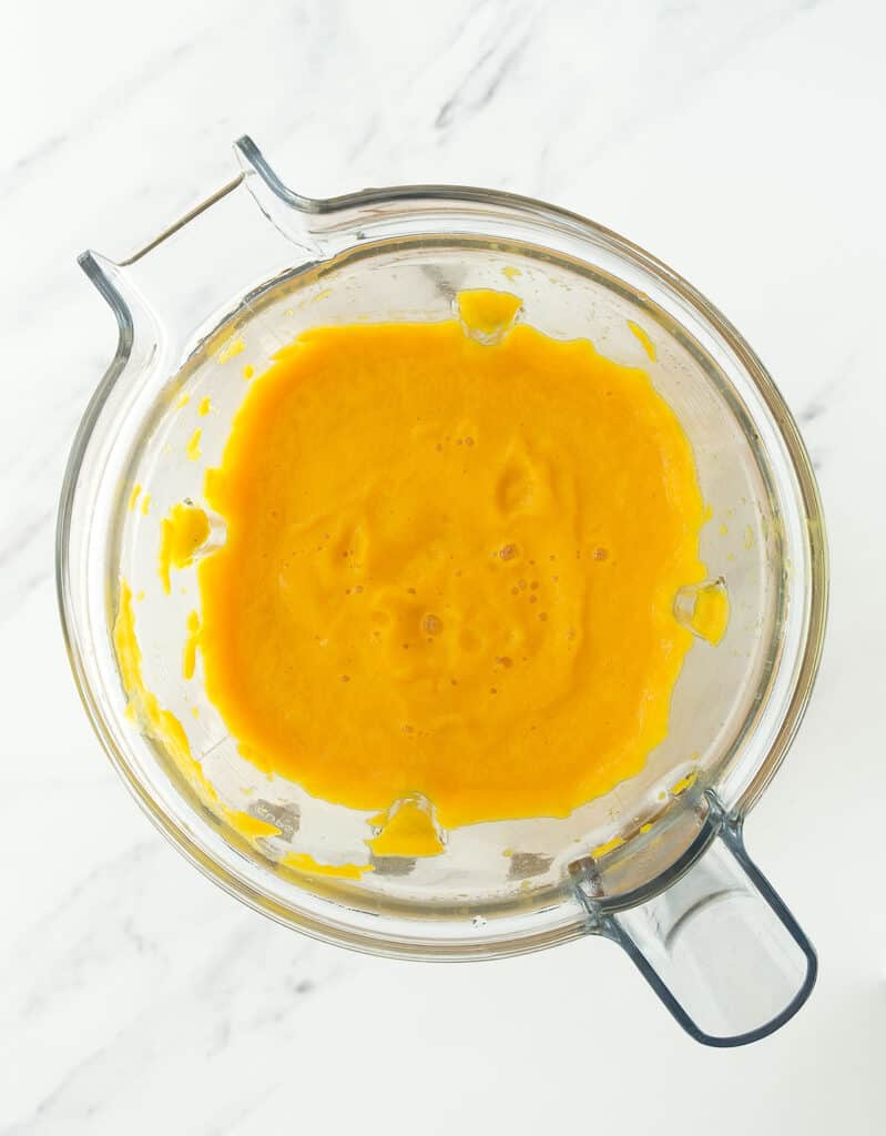 Top view of a blender full of creamy carrot and ginger soup.