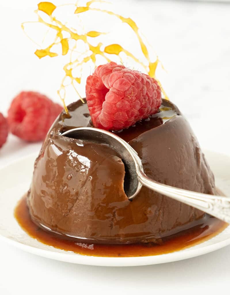 Close-up of a spoon taking a bite of chocolate pudding decorated with a raspberry. 