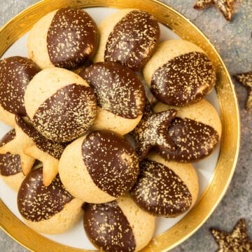 Top view of a golden plate full of chocolate dipped orange cookies decorated with golden dust.