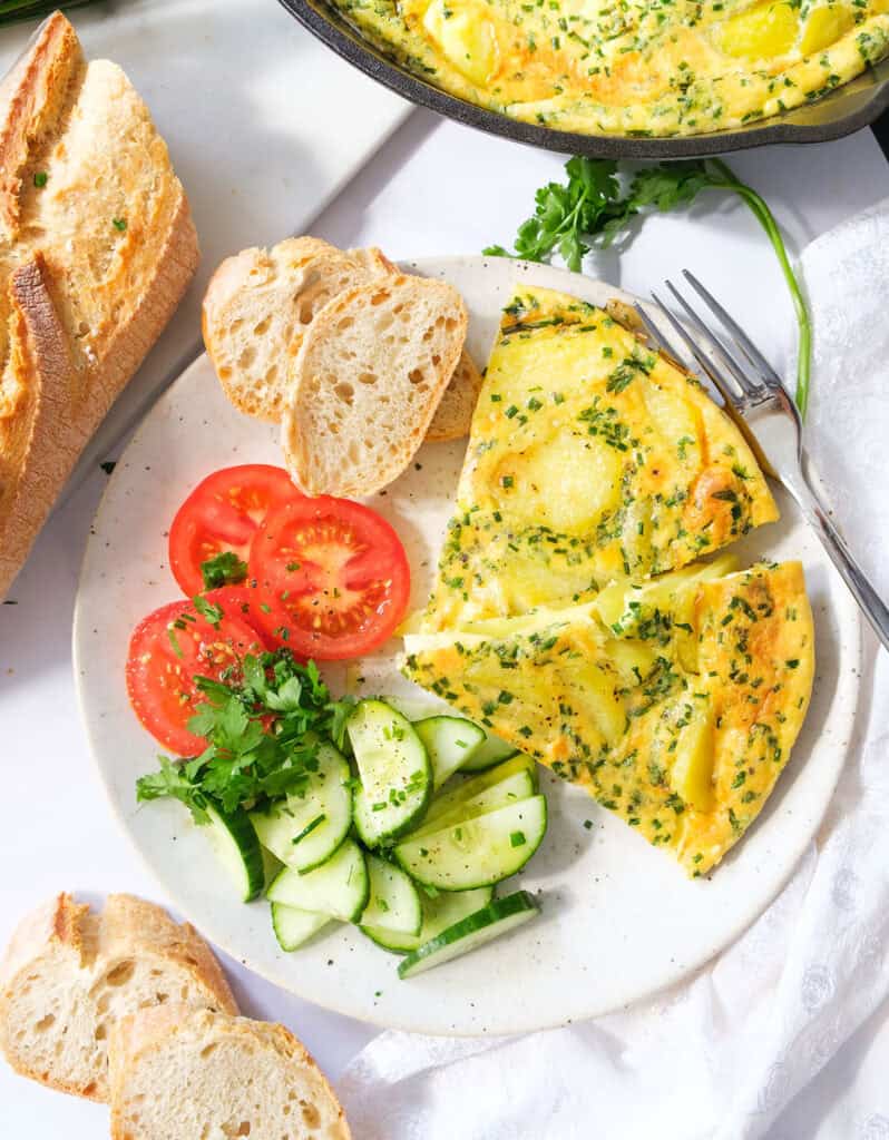 Top view of a plate with two slices of potato frittata and some salad and bread on the side.