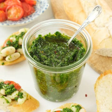 A glass jar full of green parsley pesto with a spoon.