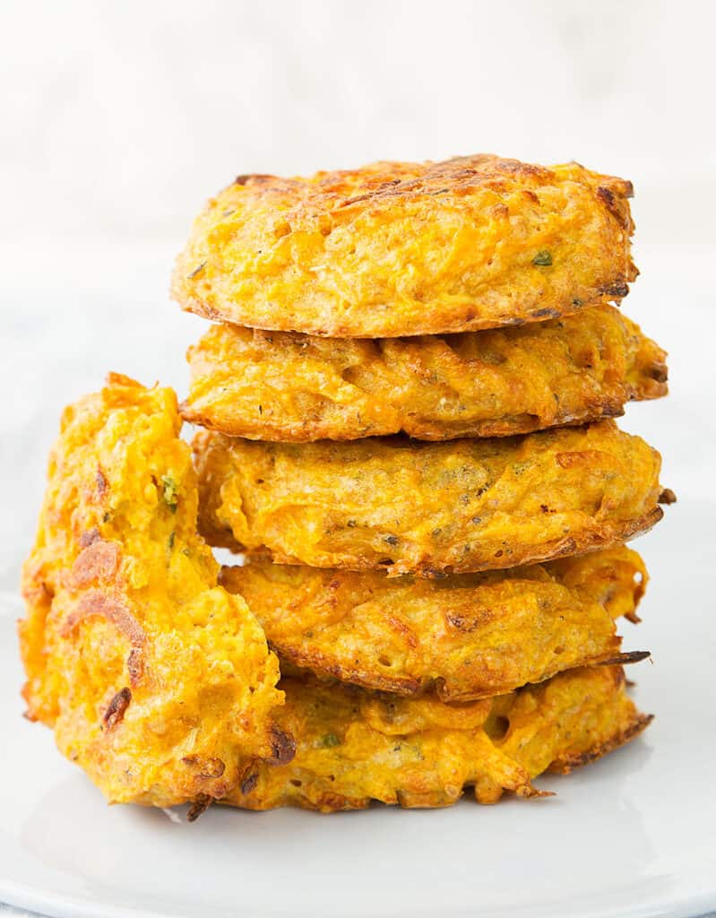 Close-up of a pile of crispy butternut squash fritters over a white background.