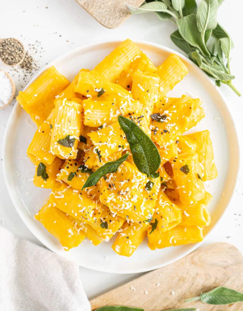 Top view of creamy vegan pumpkin pasta on a white plate over a white background.