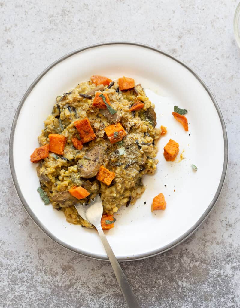Vegan risotto with roasted pumpkin cubes and herbs on a white plate by Vegan Richa.
