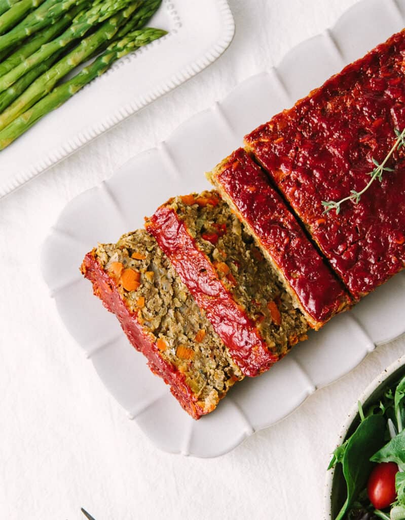 Top view of a lentil loaf cut into slices on a white tray over a white background.