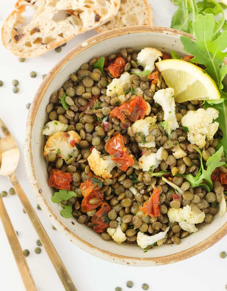 Top view of a rustic bowl full of green lentils, cauliflower bits and sun dried tomatoes.