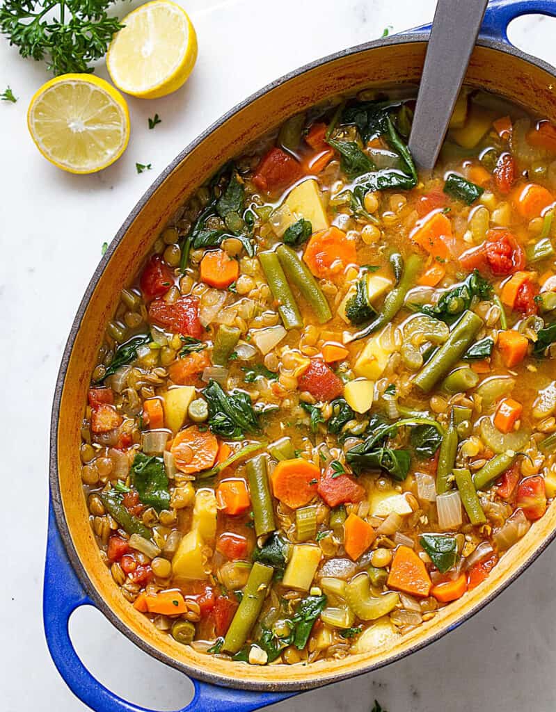 Top view of a blue oval Dutch oven full of green lentils and vegetables.